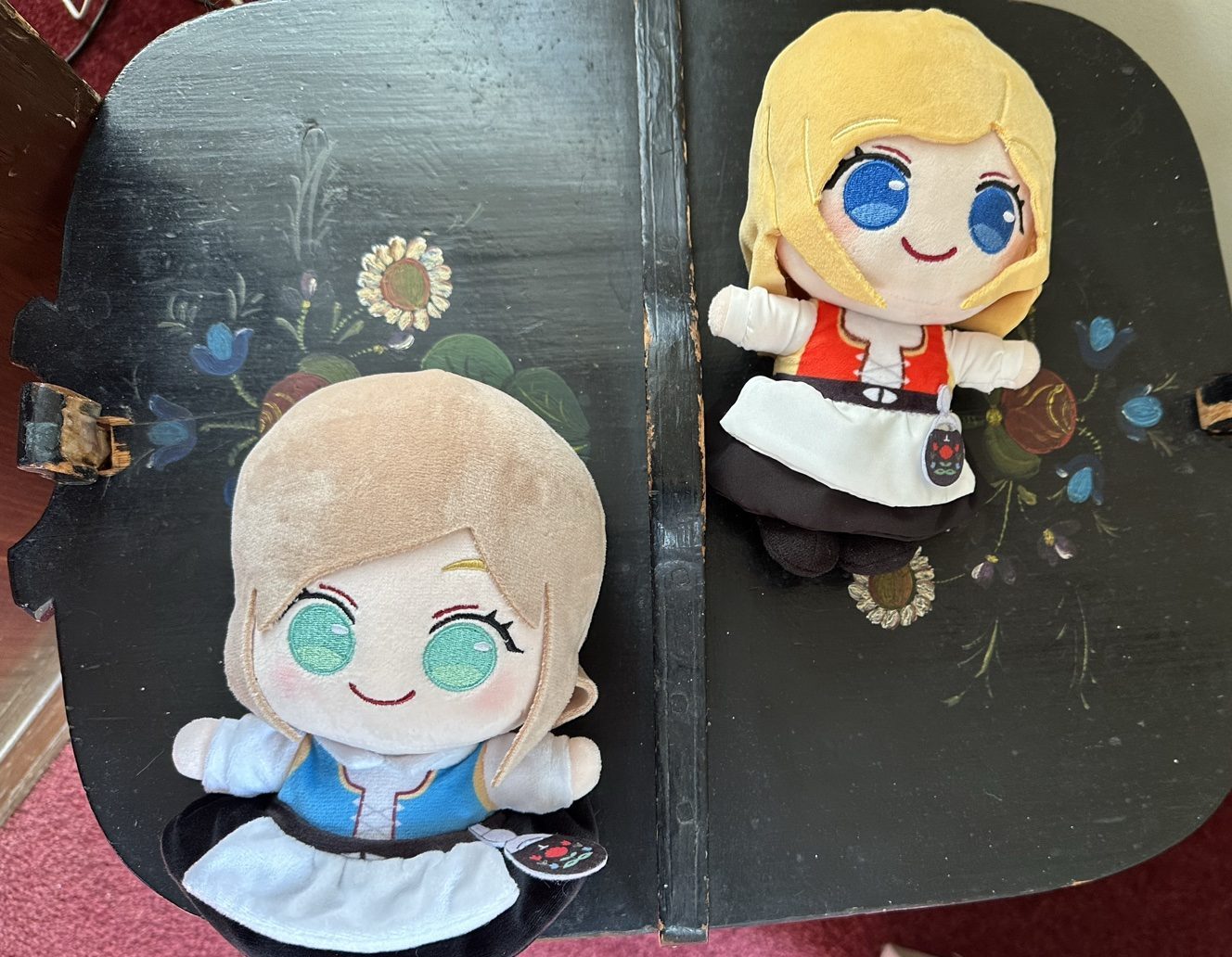Two BestaJuni plush dolls in Norwegian bunad sitting on a hand-painted rosemaling bench